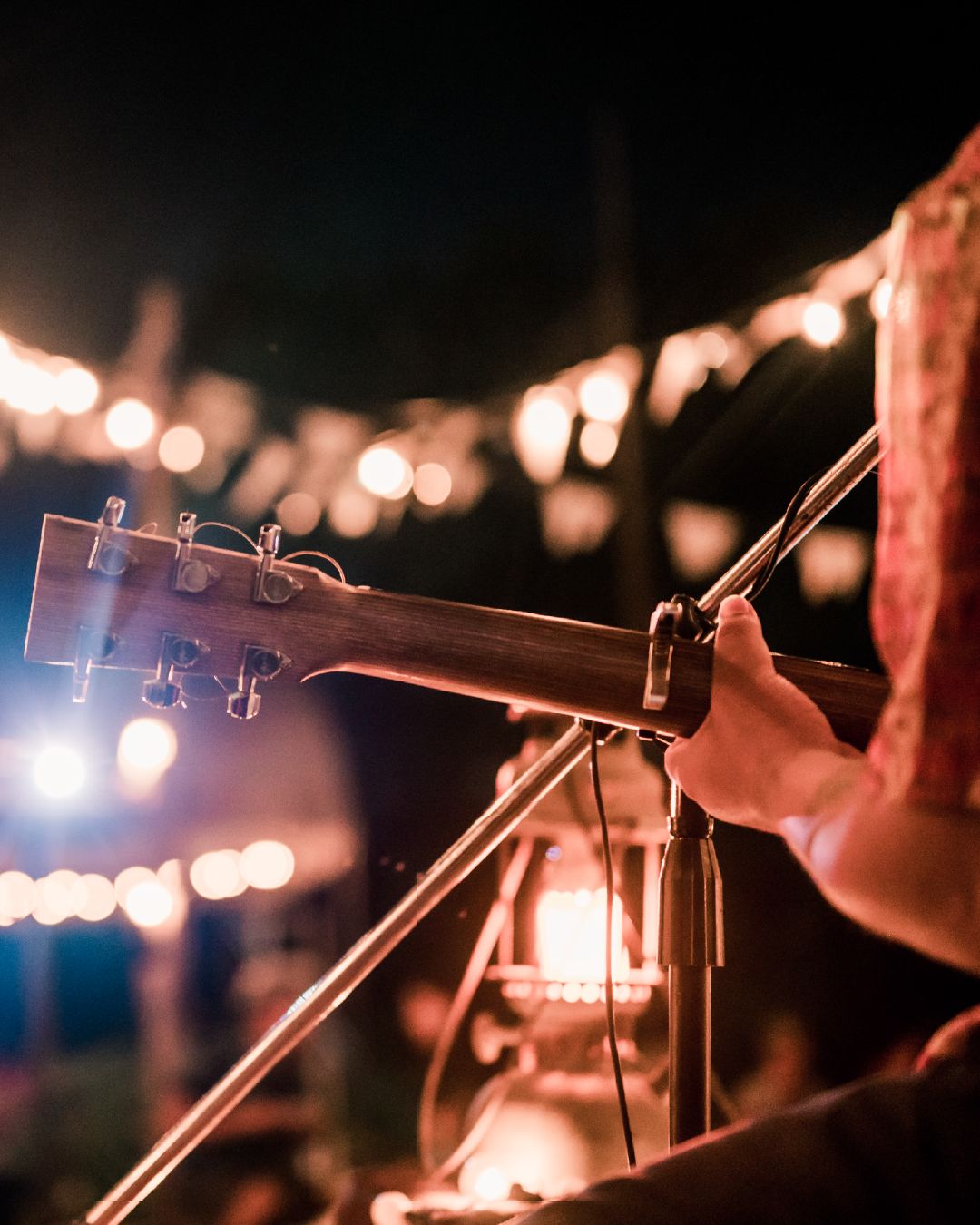 A person playing guitar on stage with fairy lights in the background. 