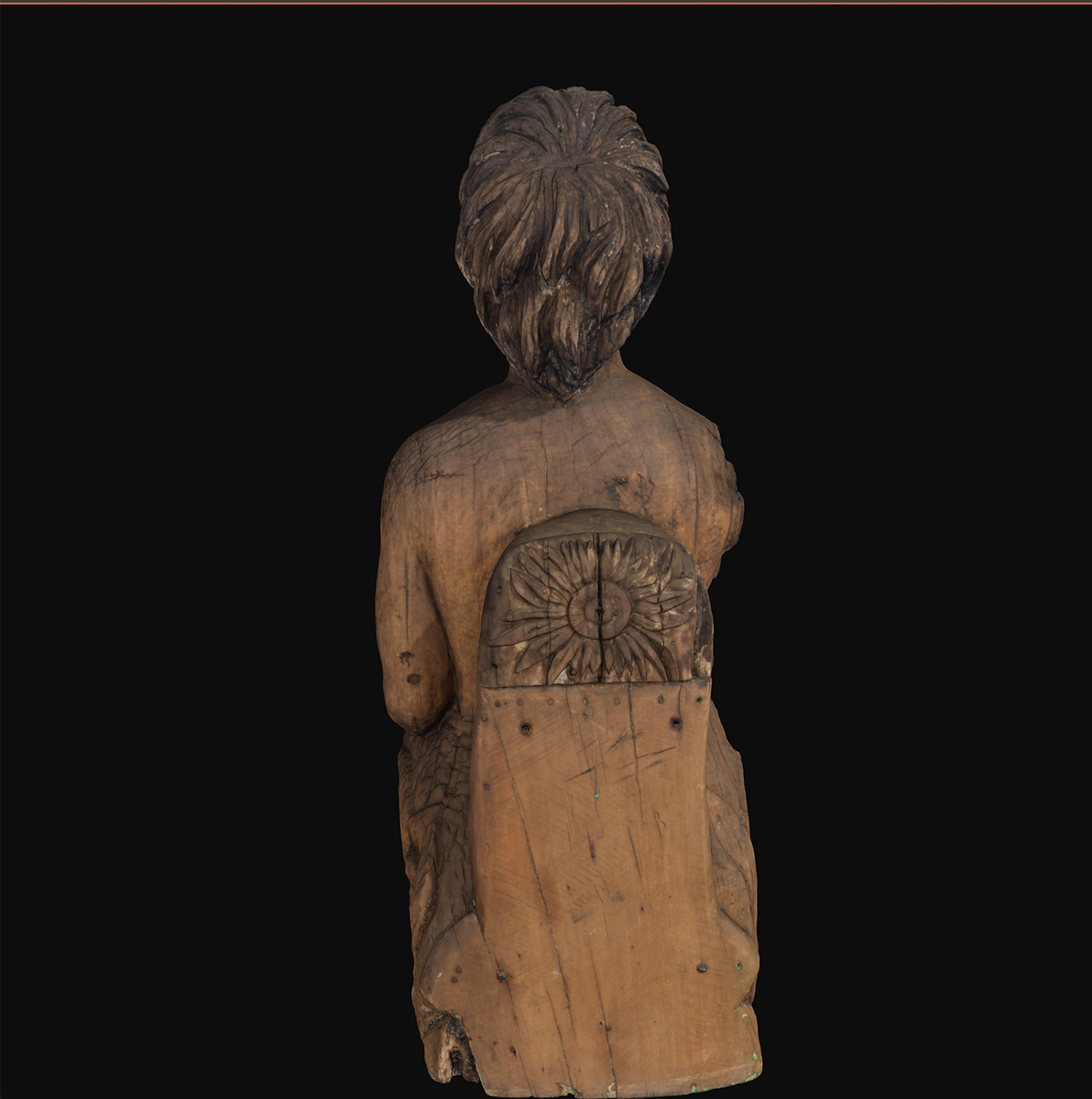 : Back view of the wooden figurehead representing a First Nations woman, with native Australian floral motifs visible. Figure against a black background.