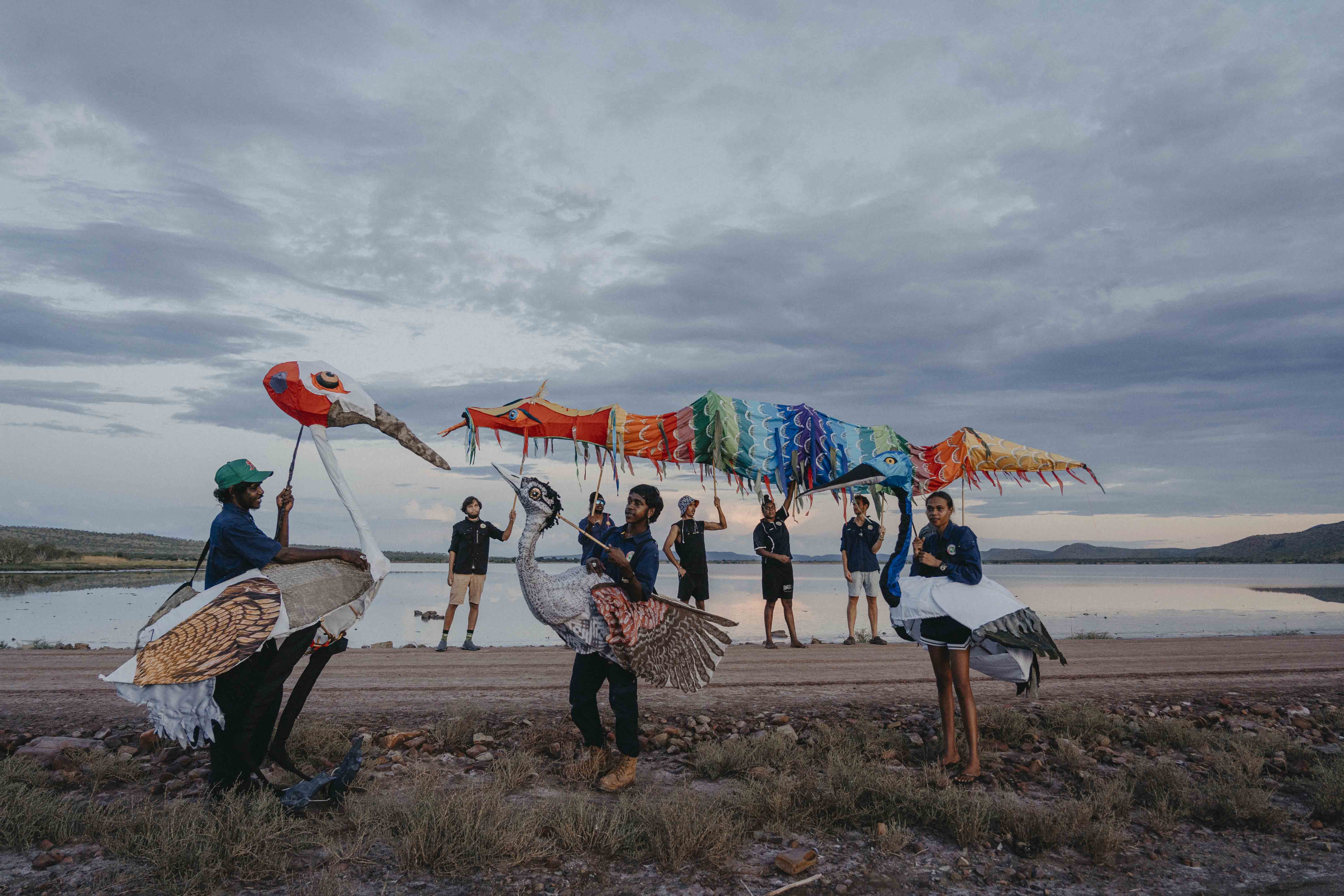 A group of people on a beach showcasing vibrant puppetry that features First Nations designs. 