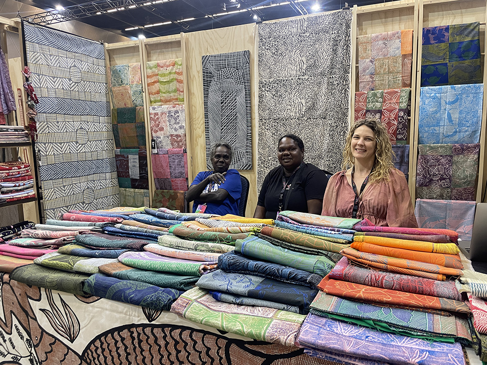 three women at a stall displaying textiles