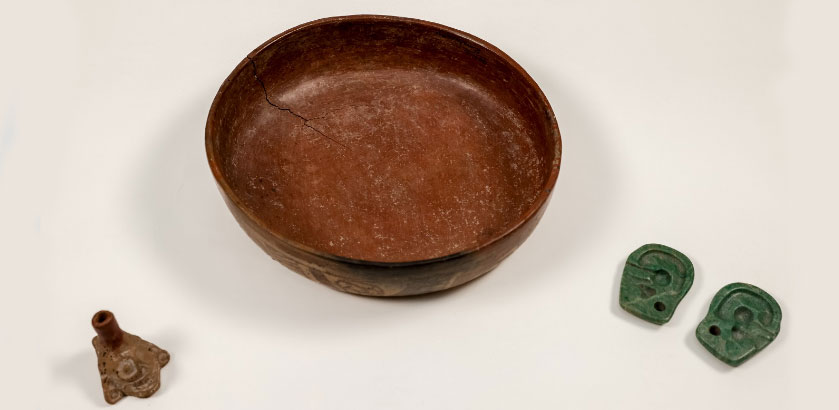 Three cultural objects from Mexico—a ceramic whistle, a ceramic bowl, and 2 green plaques resembling ears. 