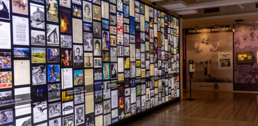 An exhibition space with a backlit wall showing a collage of images of collection items from the National Archives of Australia.
