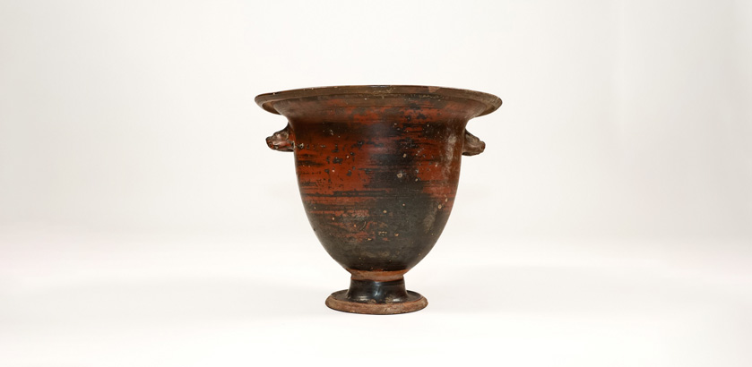 An ancient ceramic vase with black and red colouring and animal head-shaped handles. 