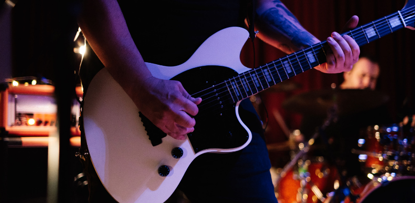 Person playing a white electric guitar on stage.