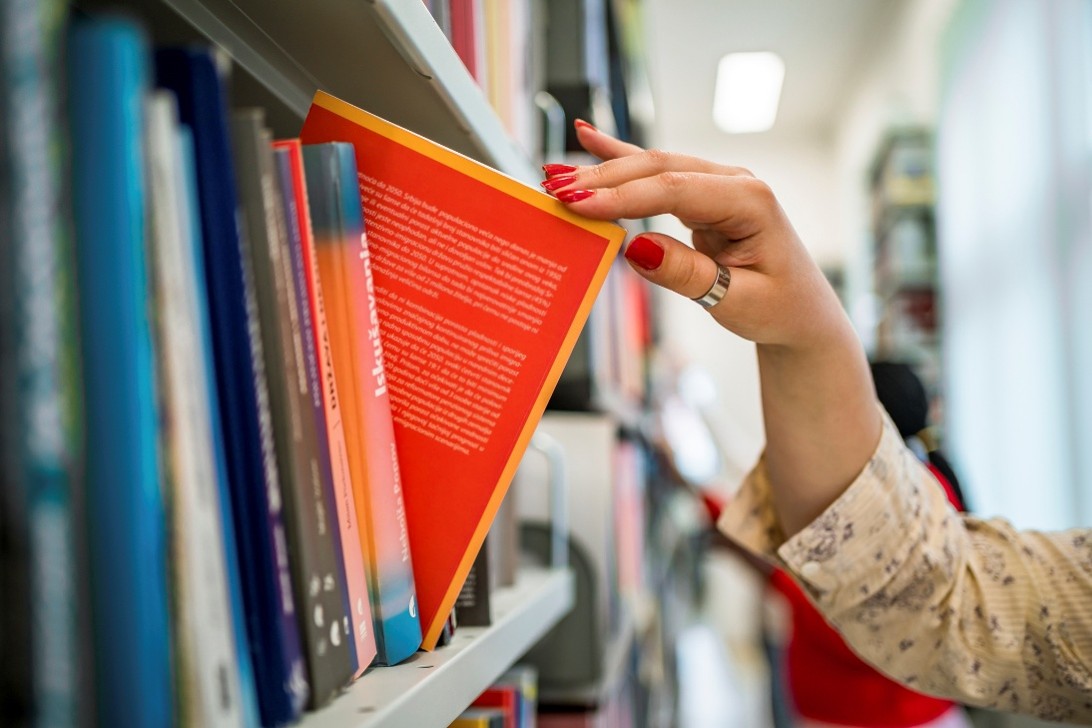 A person’s hand slides a book out of a library bookshelf.