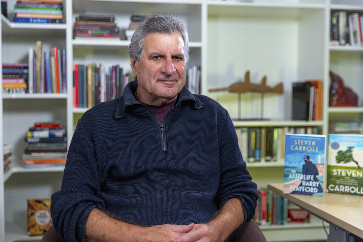 Australian author Steven Carroll sits in front of a bookcase. 