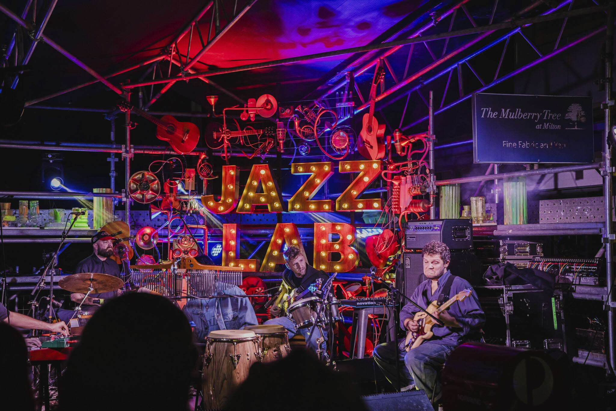 A band plays their instruments in front of a lit-up sign that reads ‘Jazz Lab’. 