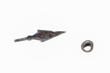 An iron arrowhead and a small round metal pendant against a white background.