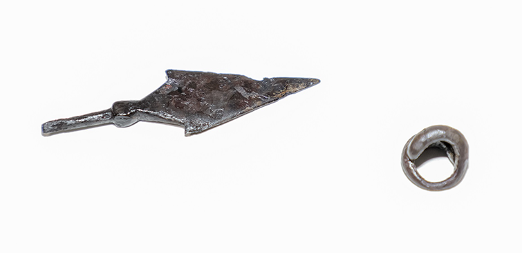 An iron arrowhead and a small round metal pendant against a white background.