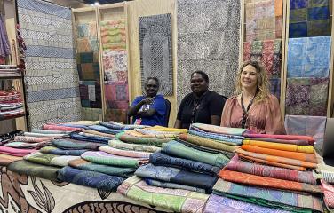three women at a stall displaying textiles