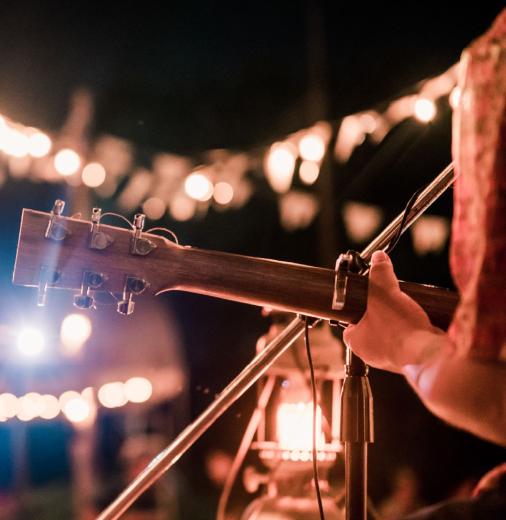 A person playing guitar on stage with fairy lights in the background. 