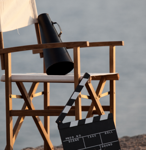 Director's chair with a megaphone sitting on it and a film board standing on the ground nearby. There is a water scene in the background. Could be a lake or sea.