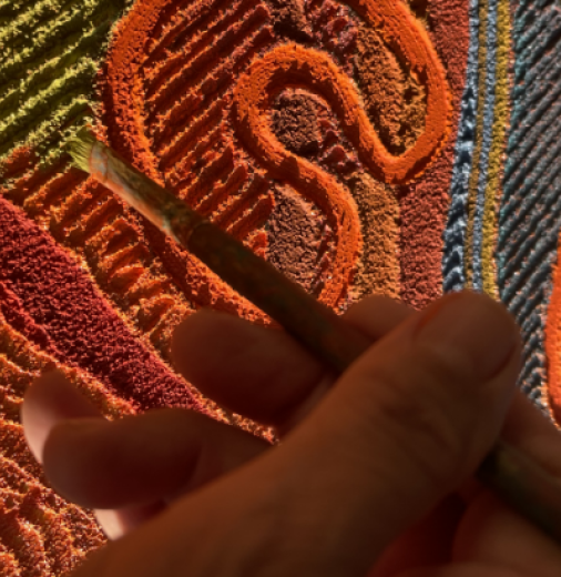 Close up of a hand holding a paintbrush against a brightly-coloured artwork