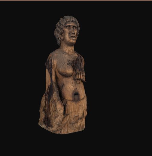 Front right side view of a wooden figurehead representing a First Nations woman against a black background. Native Australian floral motifs and relief of a kangaroo visible at its base.  floral motifs and reliefs of an emu and a kangaroo at its base.
