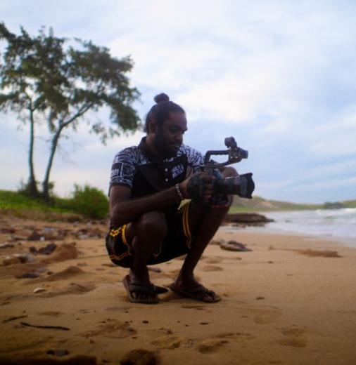 A man crouches on a beach with a film camera.