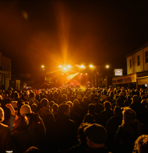 A crowd of people in the street watching Spiderbait perform on stage in Tasmania.