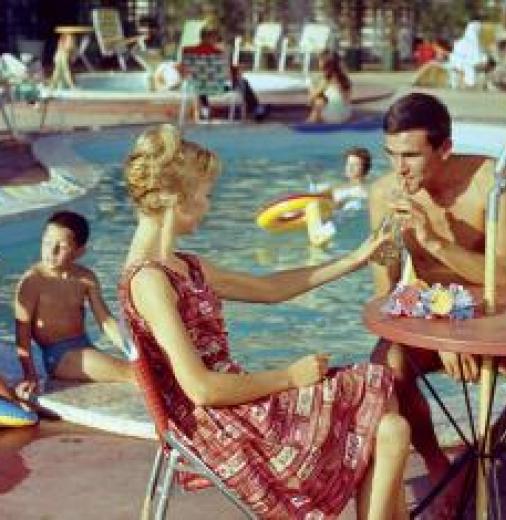Family sits by a swimming pool at a hotel in the 1960s.