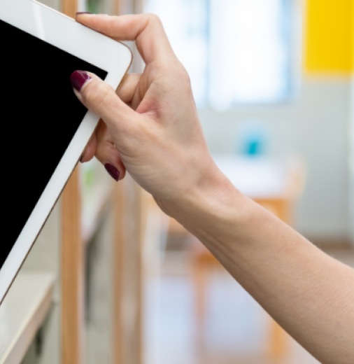 An outstretched hand from the right is pulling an ipad from a bookshelf on the left