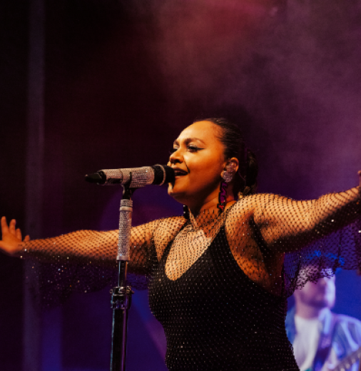 Jessica Mauboy, a First Nations woman sings into microphone on stage. 