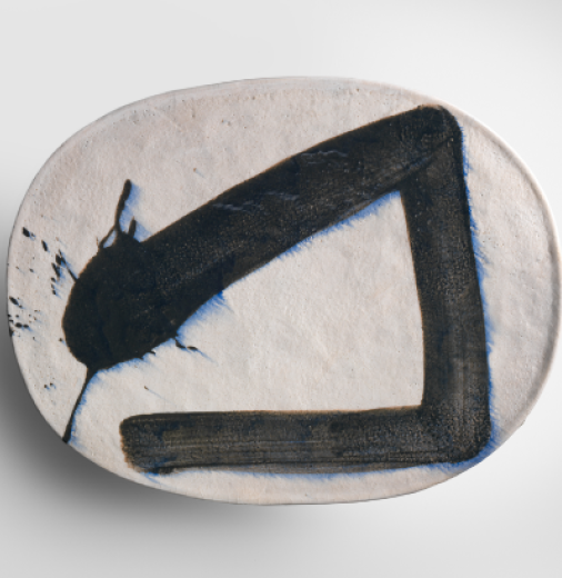 An oval ceramic piece painted with a calligraphy brushstroke sits on a white background.
