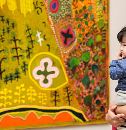 A man holding his child, while viewing an art work in a gallery