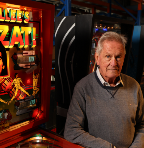 A man standing next to a pinball machine titled Dennis Lillee’s Howzat!.