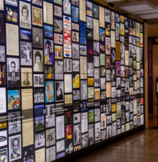 An exhibition space with a backlit wall showing a collage of images of collection items from the National Archives of Australia.