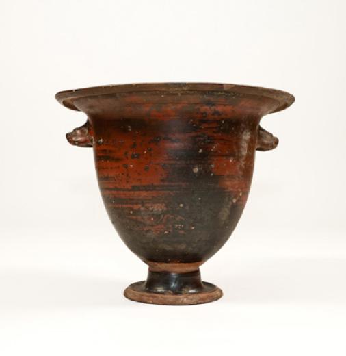 An ancient ceramic vase with black and red colouring and animal head-shaped handles. 