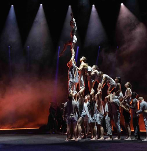 Theatre performers in a human pyramid with two people looking on from a distance.