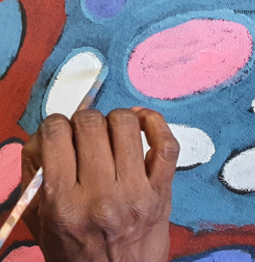 Mornington Island Arts’ artist’s hand holding a paintbrush working on a painting.