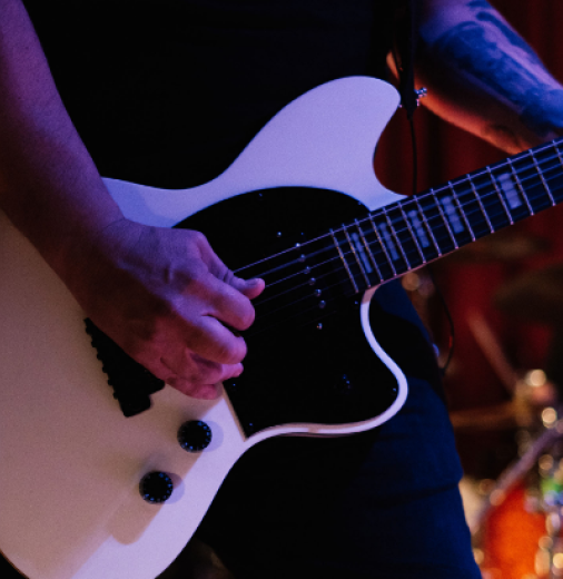 Person playing a white electric guitar on stage.