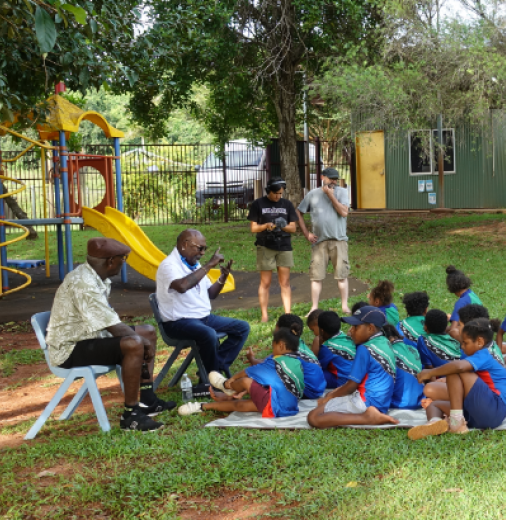 School children sit on the grass in front of a teacher during a language class. 