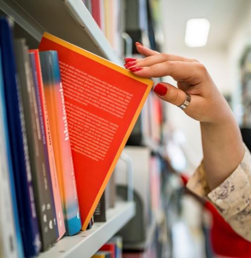 A person’s hand slides a book out of a library bookshelf.