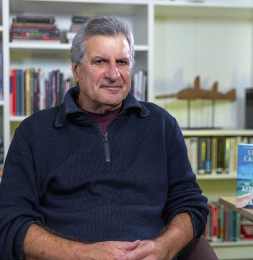 Australian author Steven Carroll sits in front of a bookcase. 