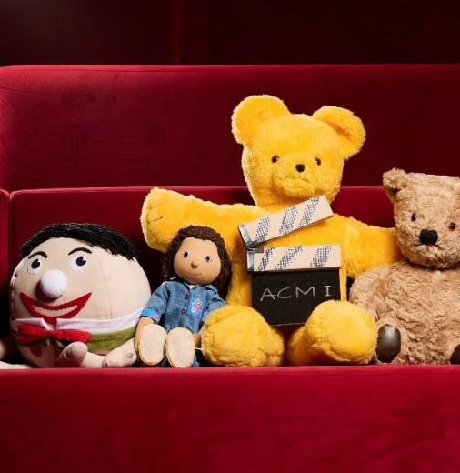 The toys from Play School sitting together in plush red cinema seats with a movie slate that reads ‘ACMI’. 