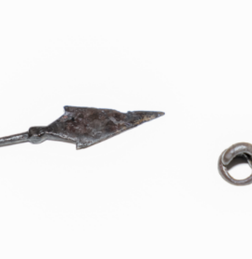 An iron arrowhead and a small round metal pendant against a white background.
