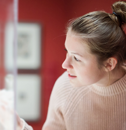 A woman peers into a cabinet with a statue inside. 