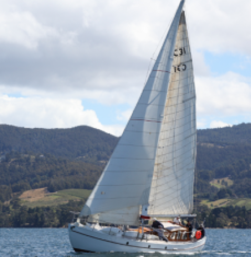 A small white boat sails on the Derwent river in Tasmania. The boat is the SV Westward.
