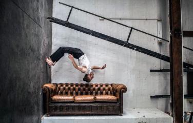 Performer above leather couch in warehouse, Flying Fruit Fly Circus.