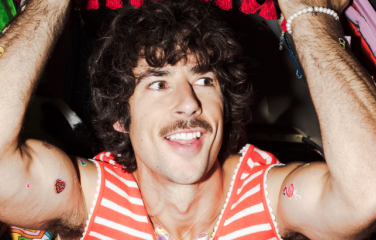 Photo of Australian music artist Go-Jo. He is wearing a red and white striped sleeveless shirt and has his arms raised.