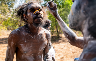 Clan junggay (Cultural leader from opposite moiety) being painted up for Mun-jiburay bunggul (performance). The yellow line represents the Balkarranga clan totem Rajarra (Barramundi).