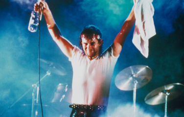 Jimmy Barnes on stage after performing with his arms raised to the audience, holding a bottle of water and towel. 