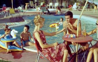 Family sits by a swimming pool at a hotel in the 1960s.