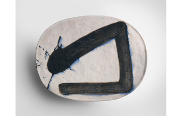 An oval ceramic piece painted with a calligraphy brushstroke sits on a white background.