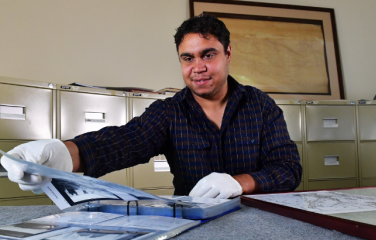 First Nations male heritage officers examines a folio of photos wearing gloves.