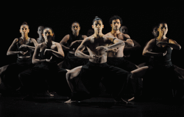 Dancers in a squatted position with there arms forming a circle in front of them.