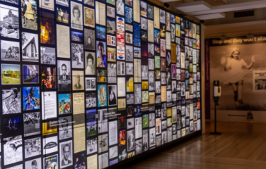 An exhibition space with a backlit wall showing a collage of images of collection items from the National Archives of Australia.