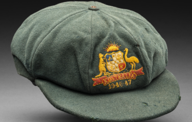 A green cricketer’s cap featuring a woven Australia emblem on the front with the dates 1946-47.