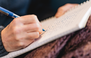 Close up of a hand writing with a pen on a lined notebook.